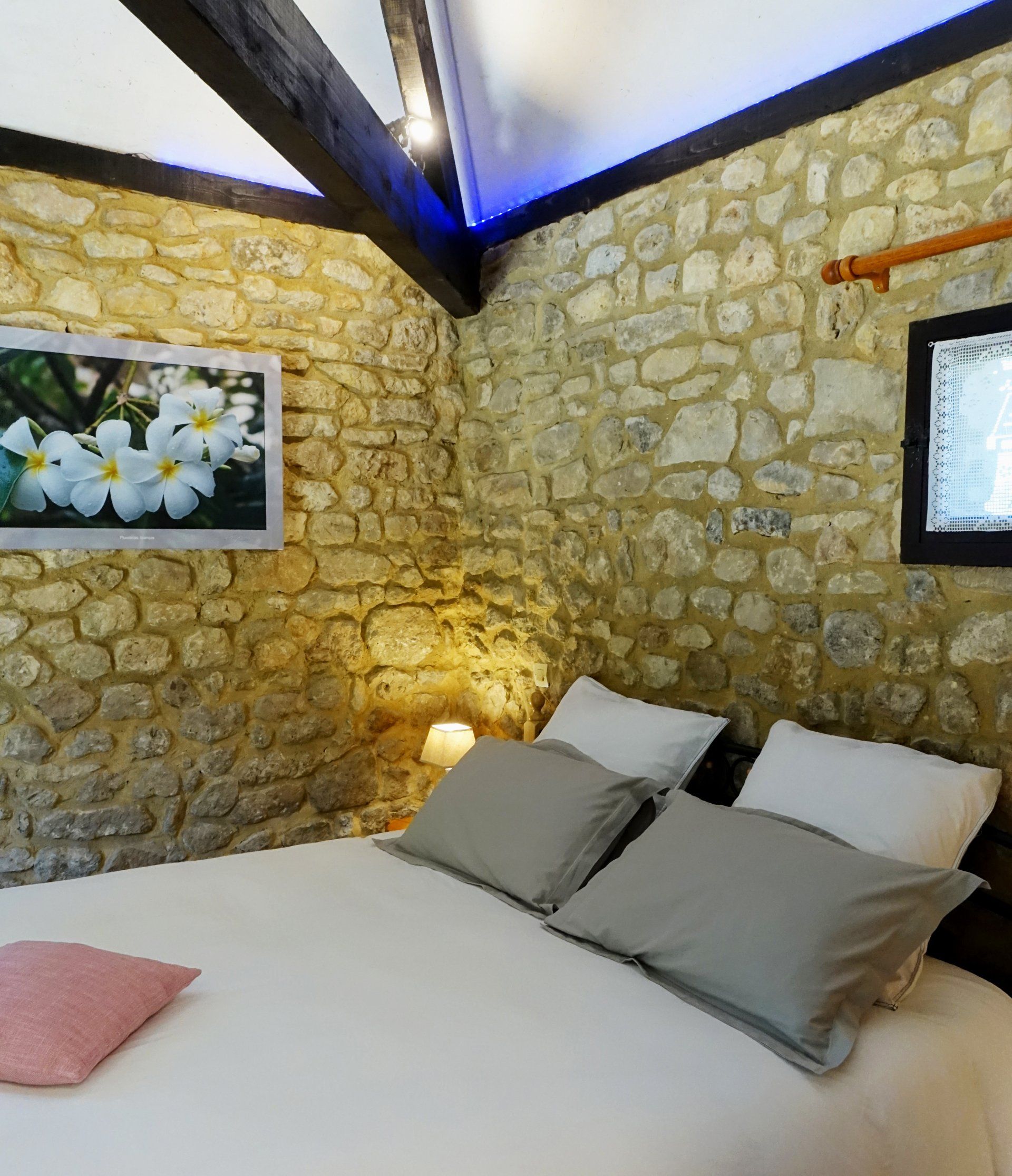Vista interior de la habitacion La Borie, la cama, foto de las flores blancas y muro de piedras. iluminacion : lampara de mesita de noche.