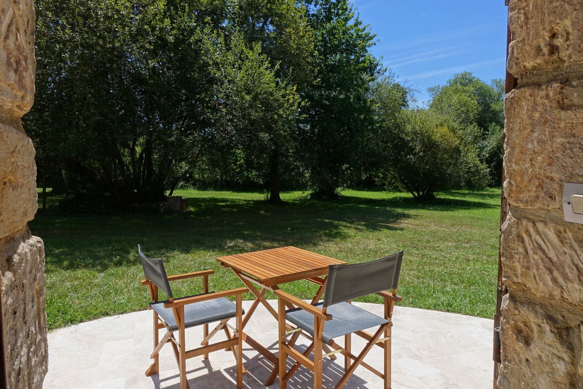 Terrasse de la chambre La Borie avec table et chaises en bois au premier plan. Vue sur les arbres et le pré