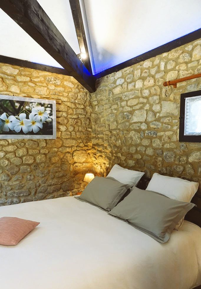 Vue intérieure de la chambre La Borie avec lit en 160x200cm, photograhie murale avec fleurs blanches (frangipanier) lumières colorées bleu au plafond et dorée sur la table de chevet.