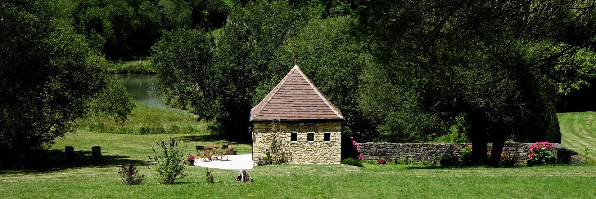 Vue panoramique de la chambre La Borie (petite maison en pierres) avec terrasse, salon de jardin en bois, pelouse, arbres
