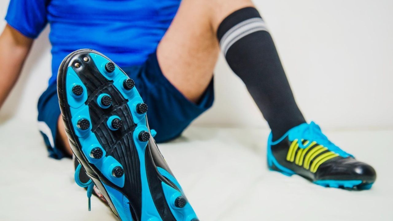 Close-up of a soccer player wearing black and blue cleats, showing the sole and studs while sitting