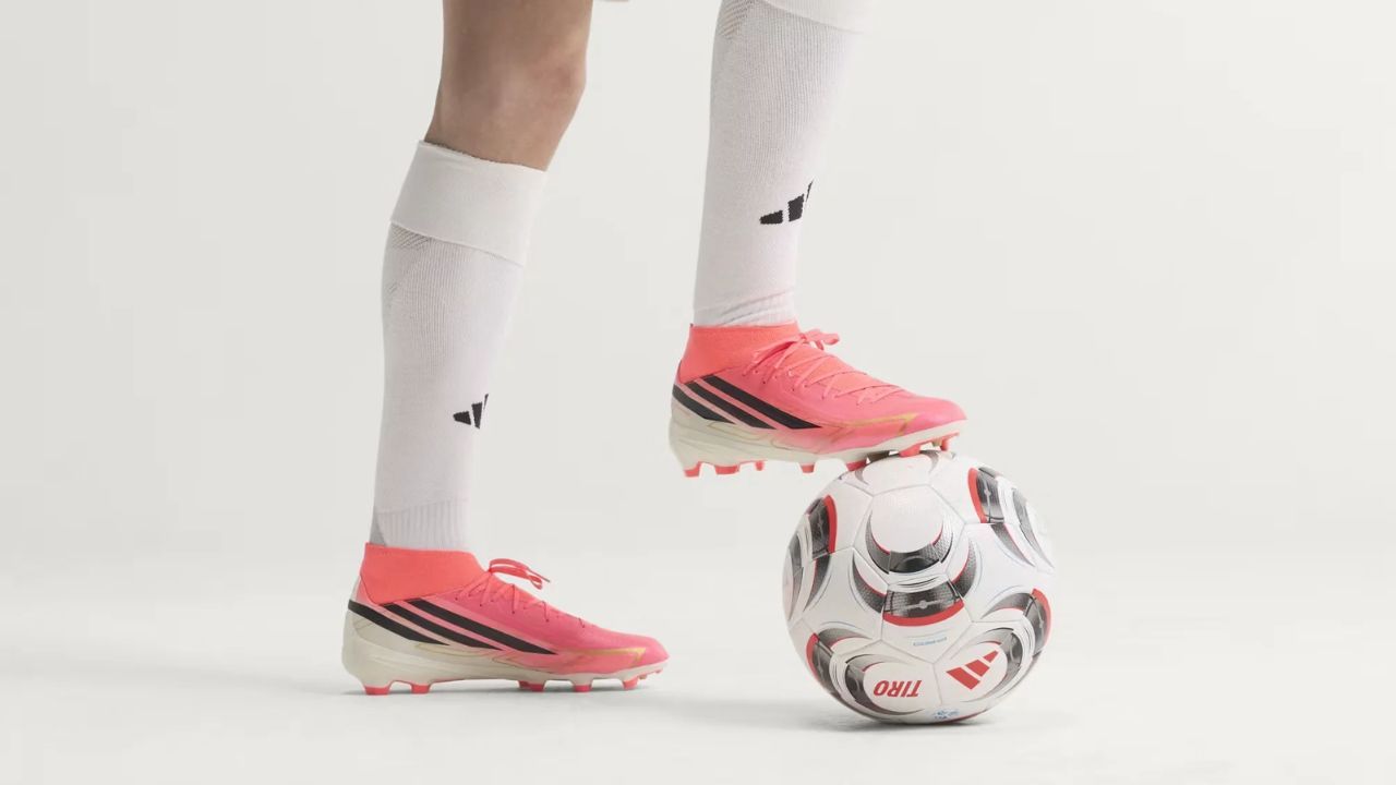 Pink soccer cleats worn with white socks beside a soccer ball.