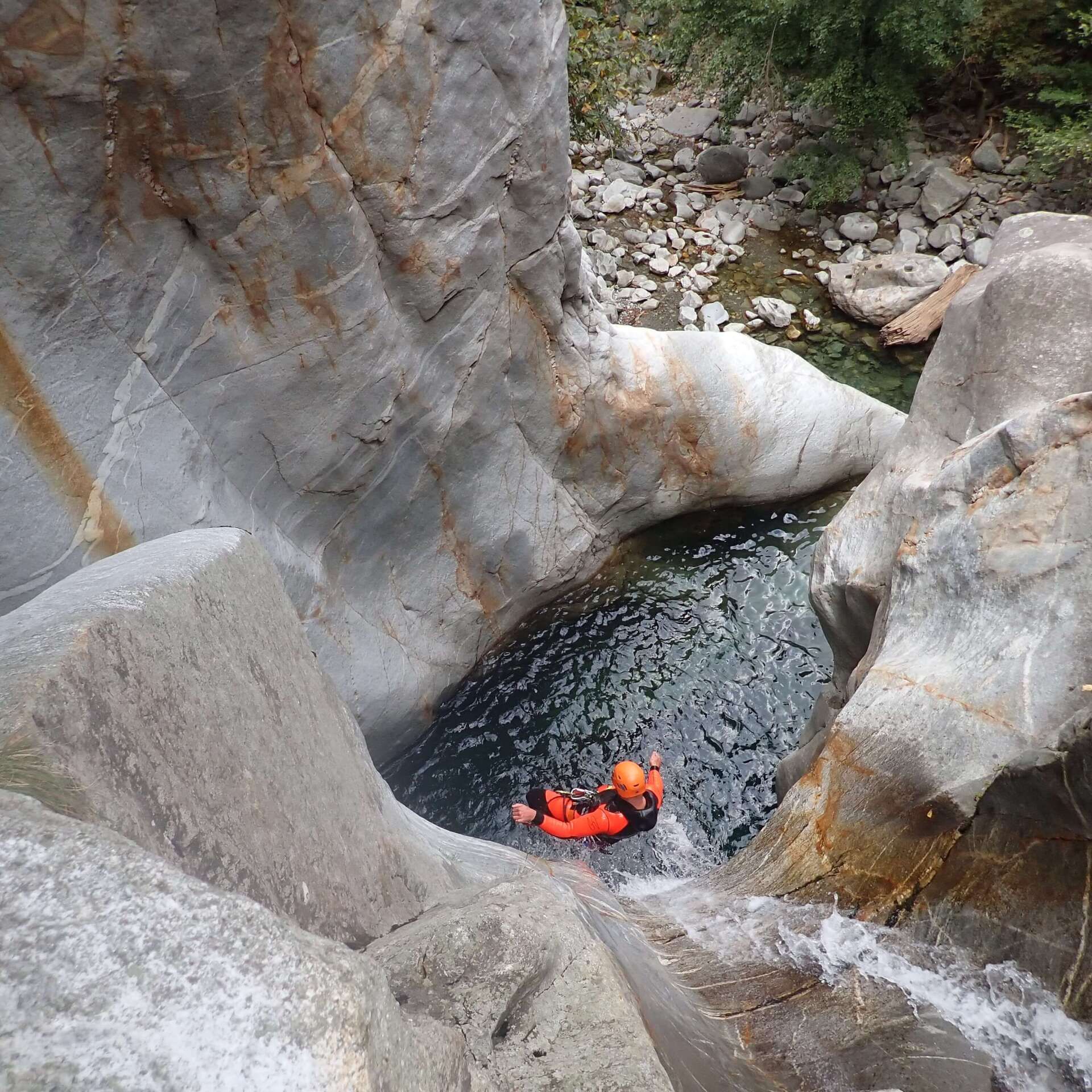 Ein männlicher Canyoning-Gast rutscht fast fliegend von einem Felsen in der Schlucht Boggera im Tessin ein Wasserbecken