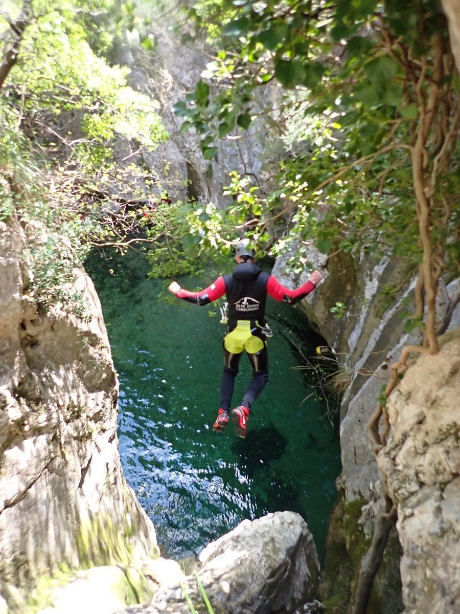 Ein Canyoning-Gast springt von einem Felsen in der Schlucht Almadra im Tramuntana-Gebirge auf Mallorca in einen natürlichen türkisen Pool mit glasklarem Wasser