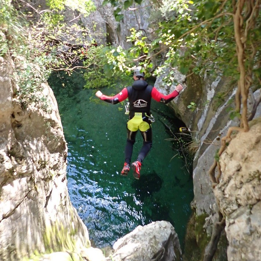 Ein männlicher Canyoning-Gast springt von einem Felsen in der Schlucht Almadra in ein grünes Wasserbecken
