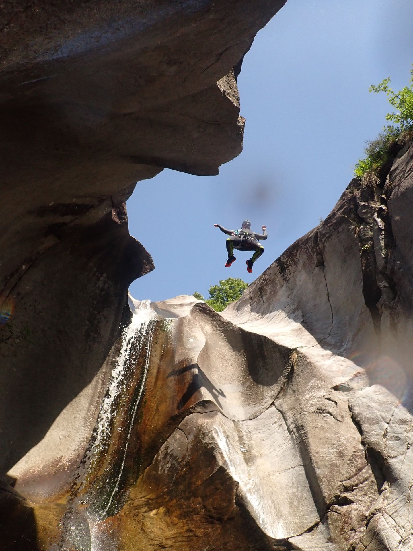 Ein Canyoninggast springt vor blauem Himmel einen Felsen in der Schlucht Boggera hinab