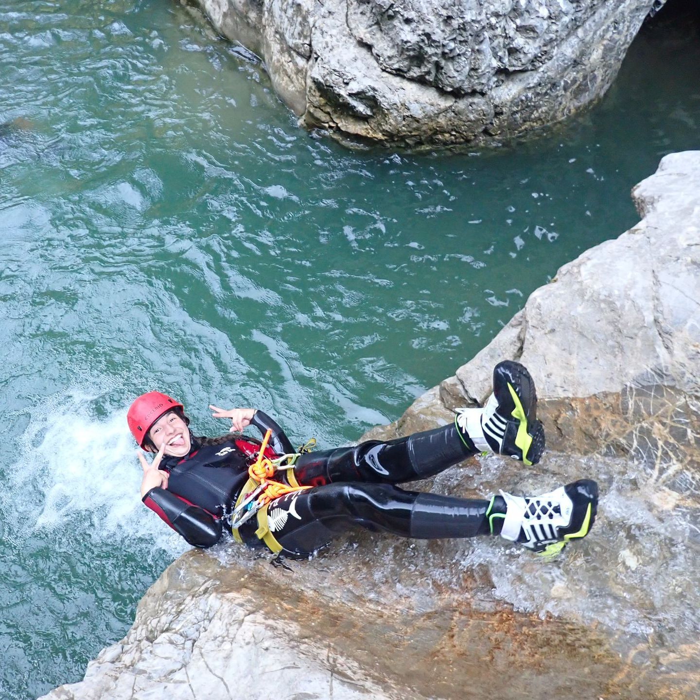 Ein weiblicher Canyoning-Gast rutscht rückwärts über einen Felsen in ein Wasserbecken der Kobelache