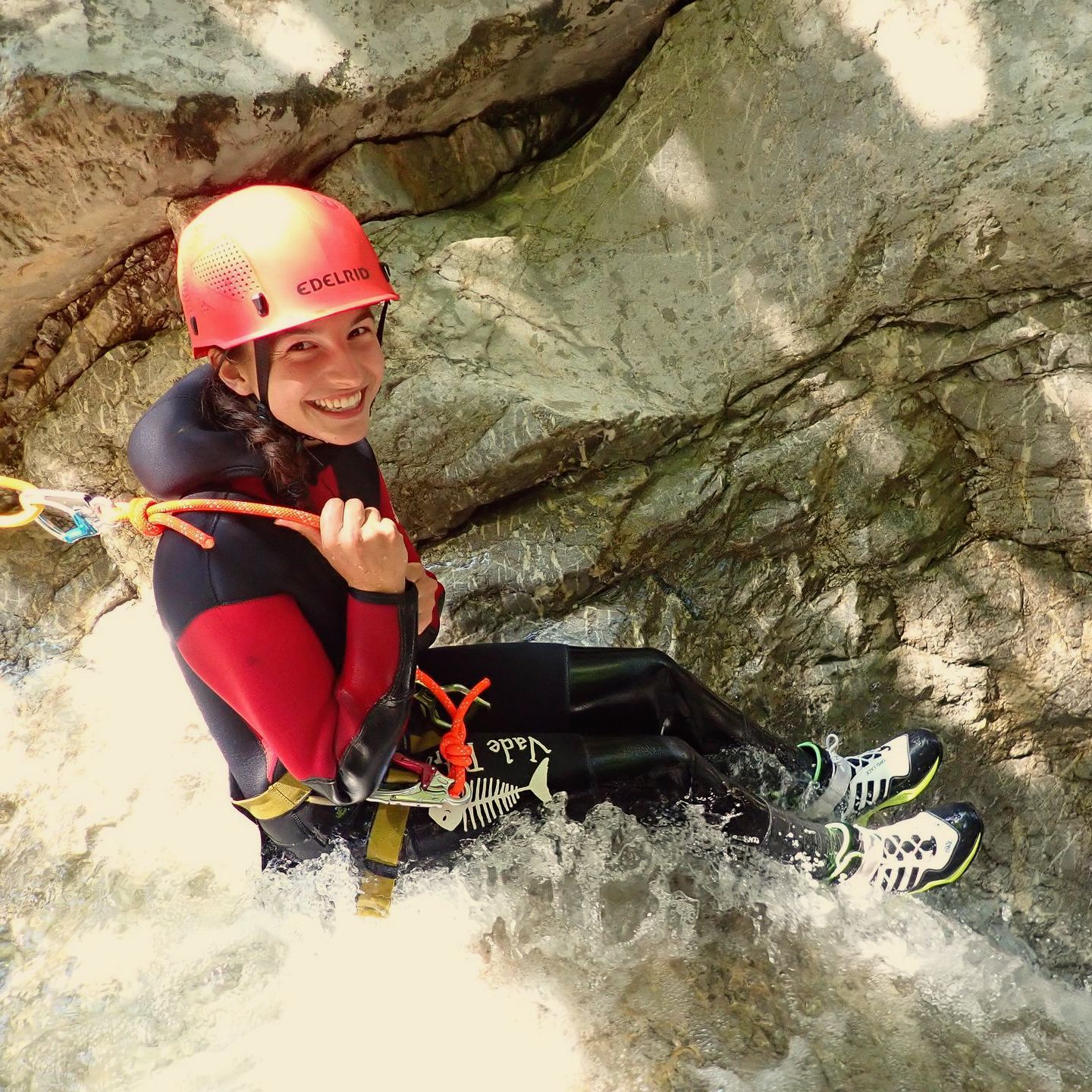 Ein weiblicher Canyoning-Gast in Vorarlberg sitzt an der Kante einer Felsrutsche und lächelt in die Kamera