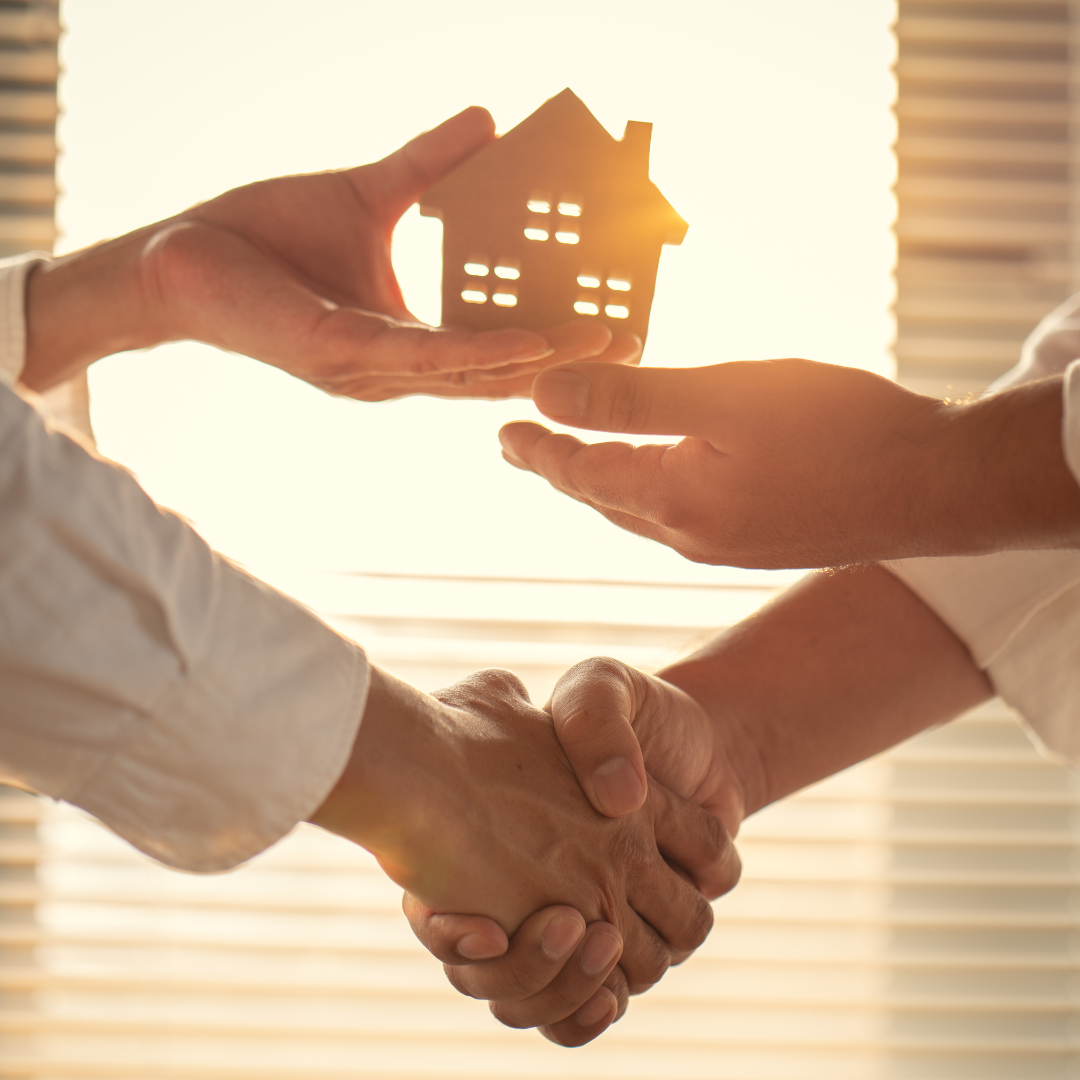 Two people shaking hands in agreement, with one person holding a small wooden house symbol, representing a successful property management deal.