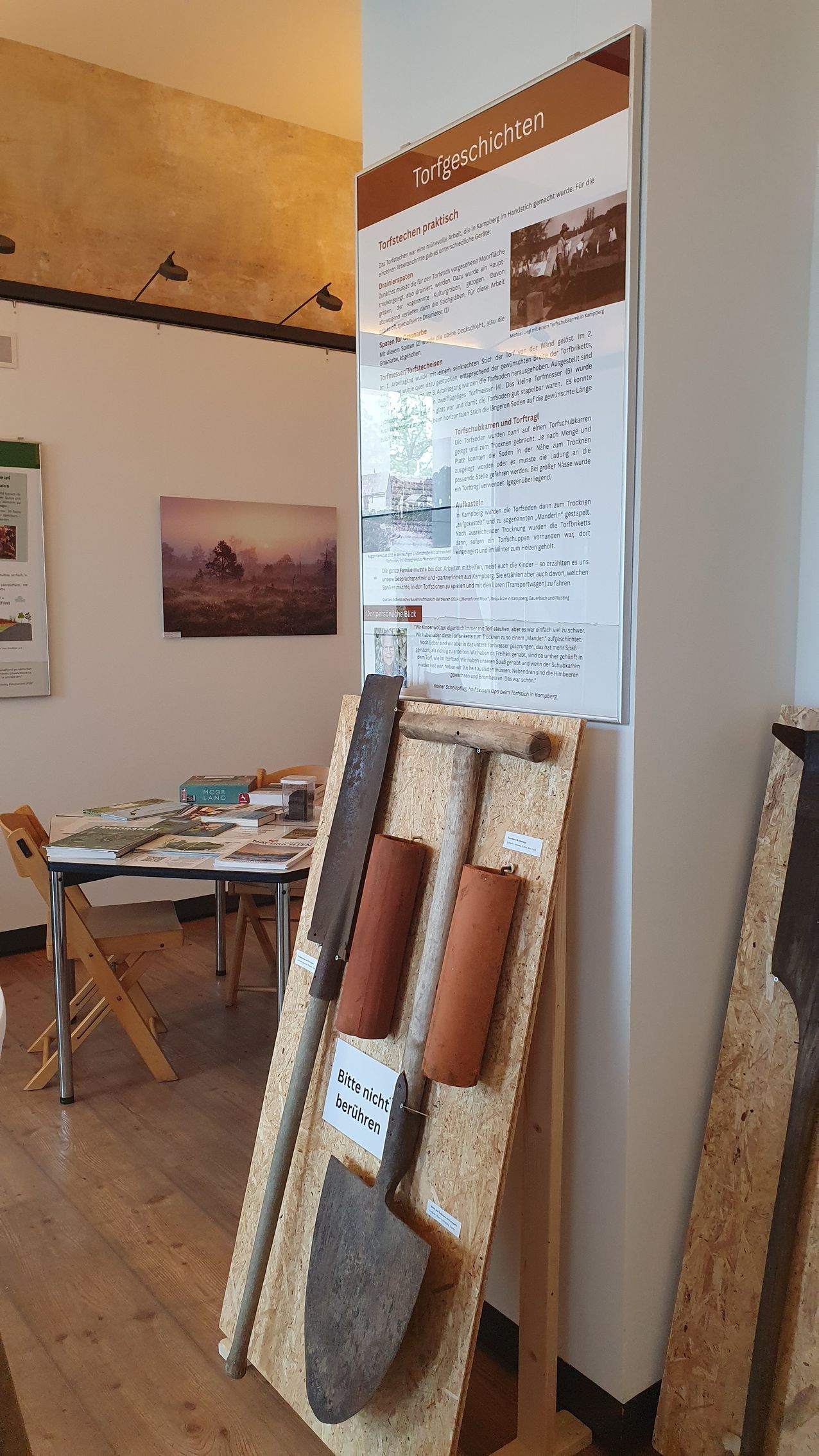 Verschiedene Geräte zum Torfstechen vor einem Plakat