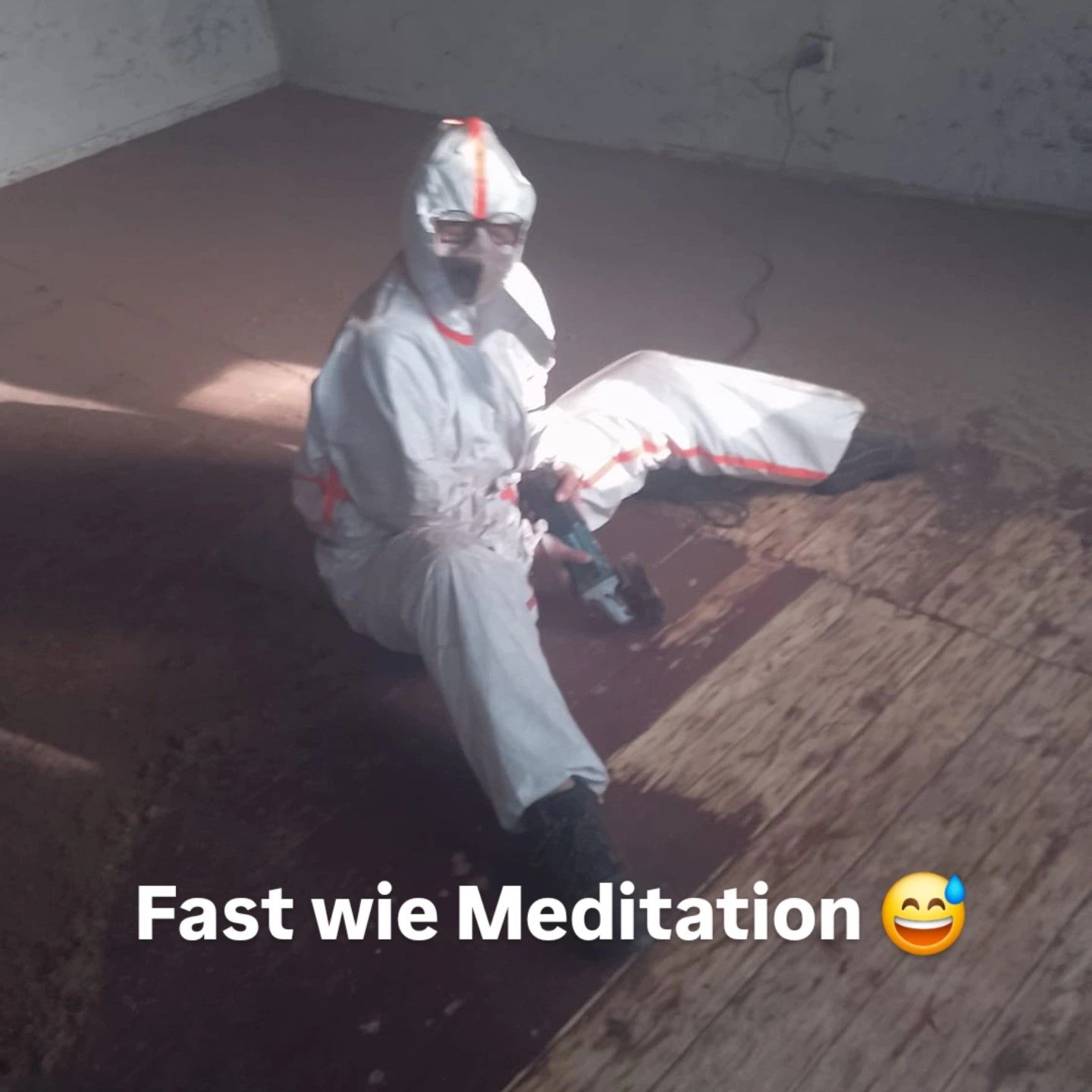 In Schutzmontur gekleideter Mensch, der auf dem Boden alter lackierter Holzdielen sitzt