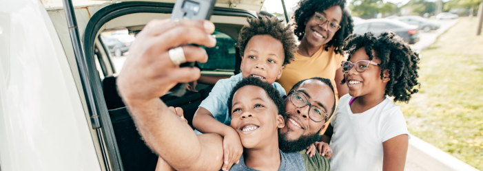 Family taking a selfie next to their vehicle