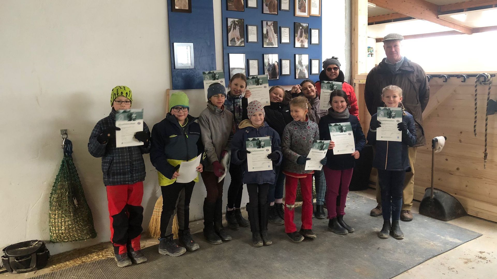 10 Kinder stehen in der Reithalle mit ihrem Reitabzeichenprüfer für ein Erinnerungsbild der bestandenen Reitabzeichenprüfung. 10 Kinder stehen in der Reithalle mit ihrem Reitabzeichenprüfer für ein Erinnerungsbild der bestandenen Reitabzeichenprüfung.