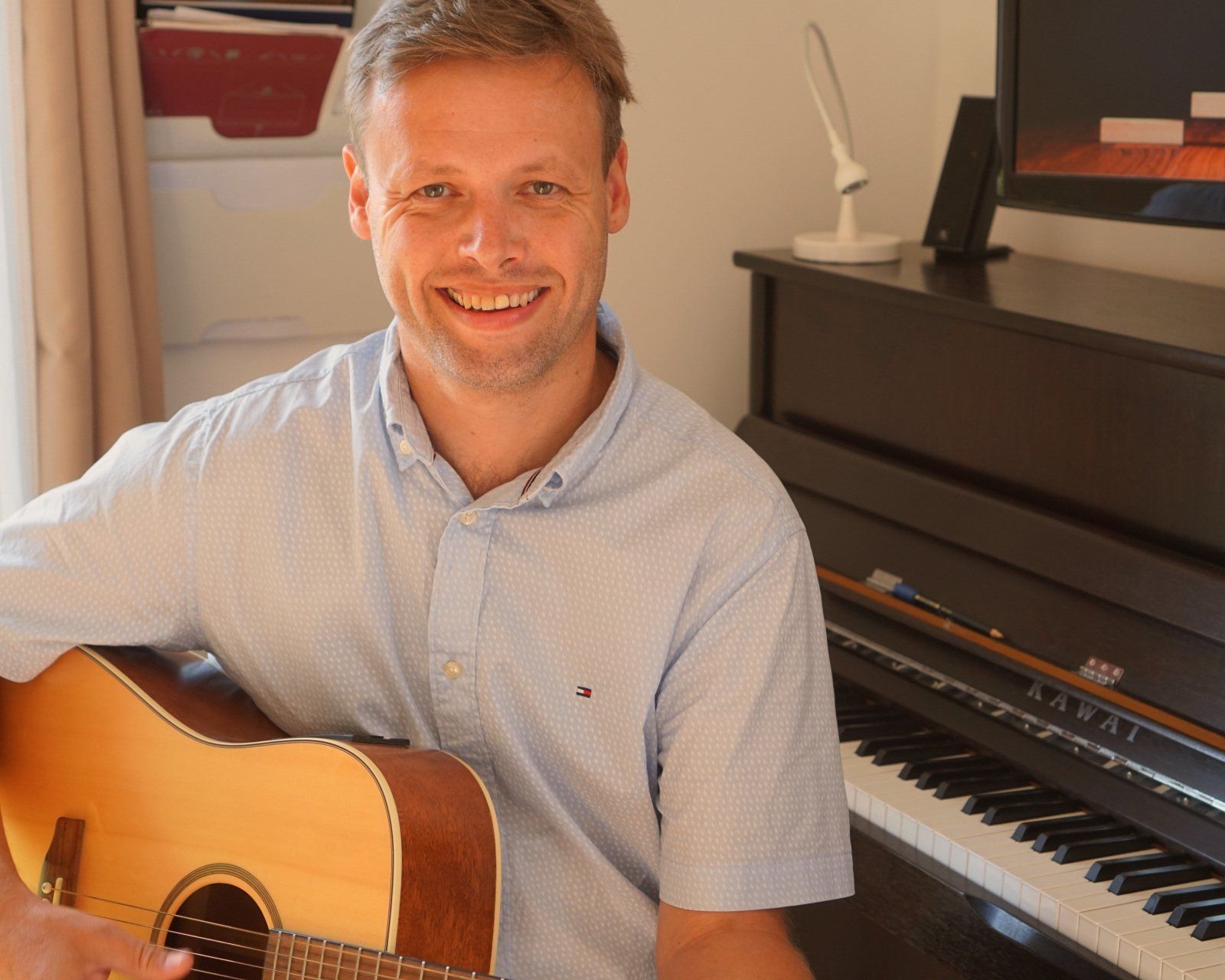 Johannes mit Gitarre vor dem Klavier im Unterrichtsraum