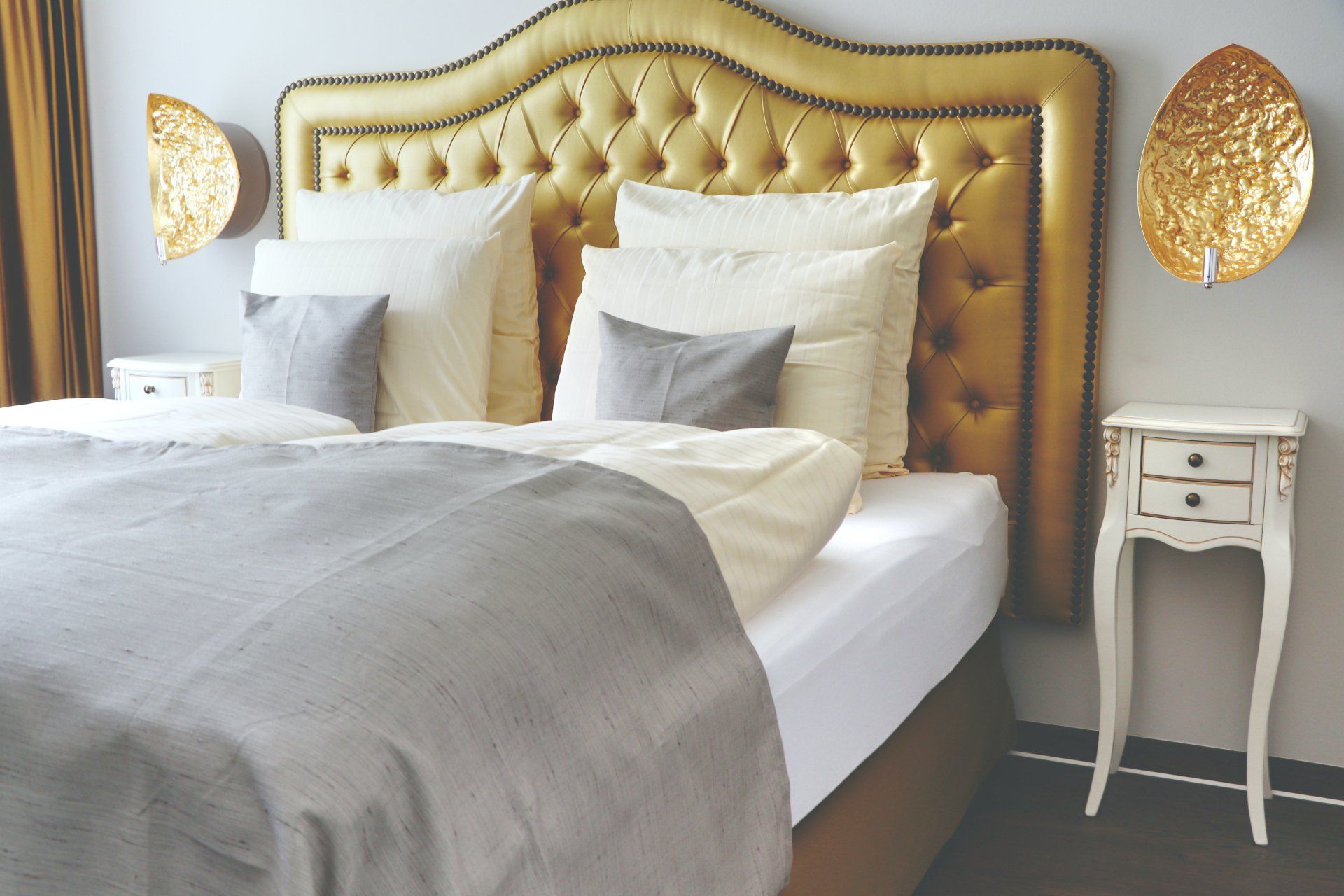 Luxuriöses Schlafzimmer mit goldener, gepolsterter Bettrückwand und eleganter Wandbeleuchtung