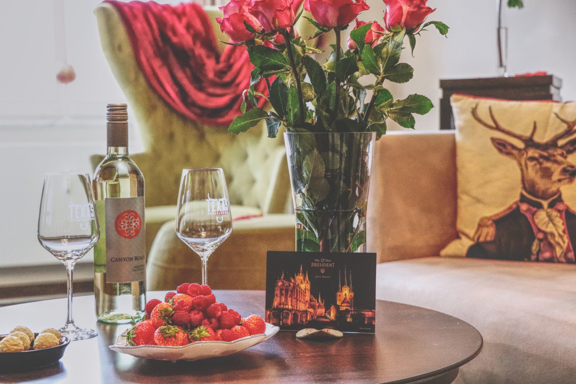 Herzliches Willkommens-Arrangement mit Wein, Erdbeeren und Grußkarte auf dem Wohnzimmertisch