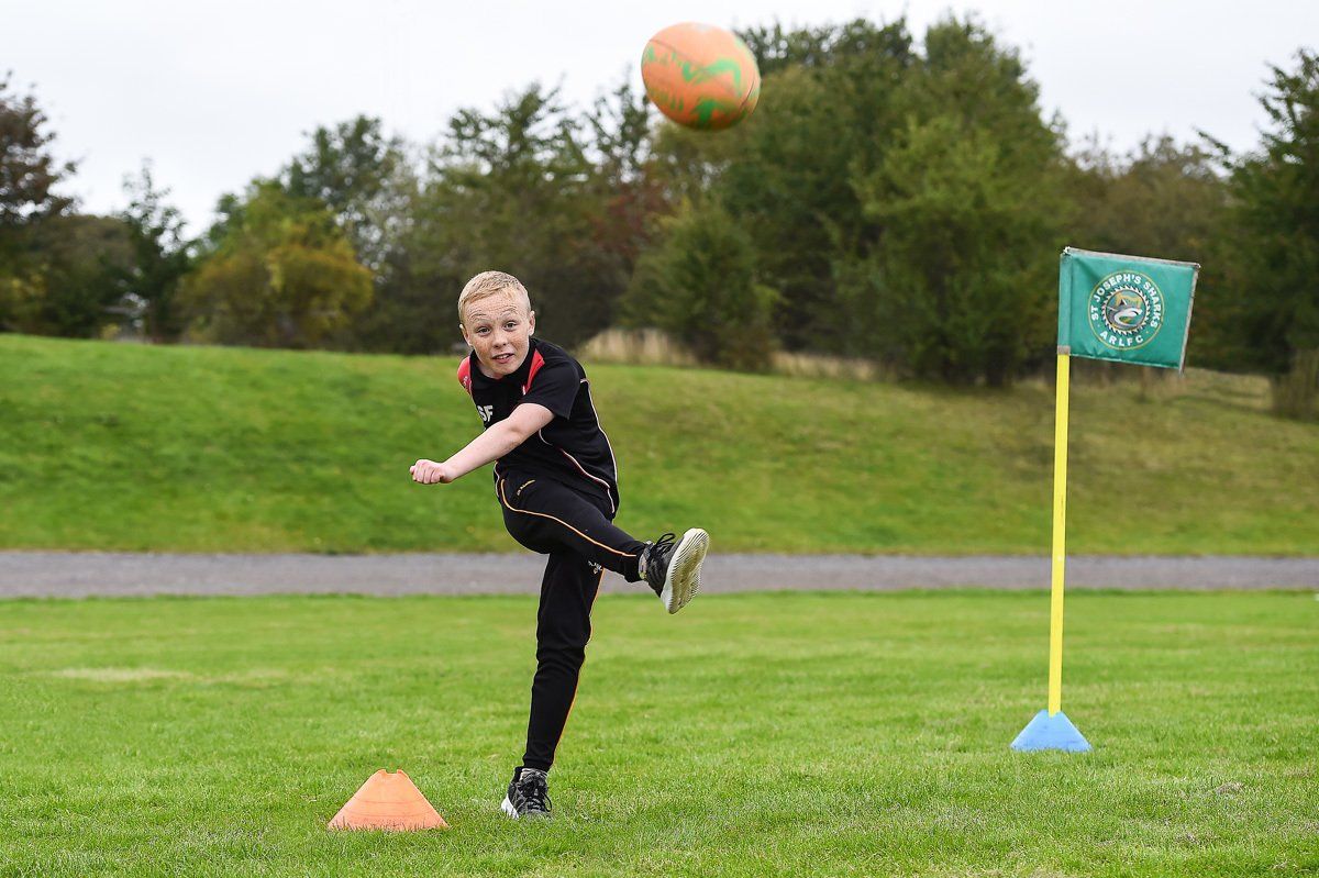 A child takes part in a community fun day in Huddersfield, and kicks a rugby ball.