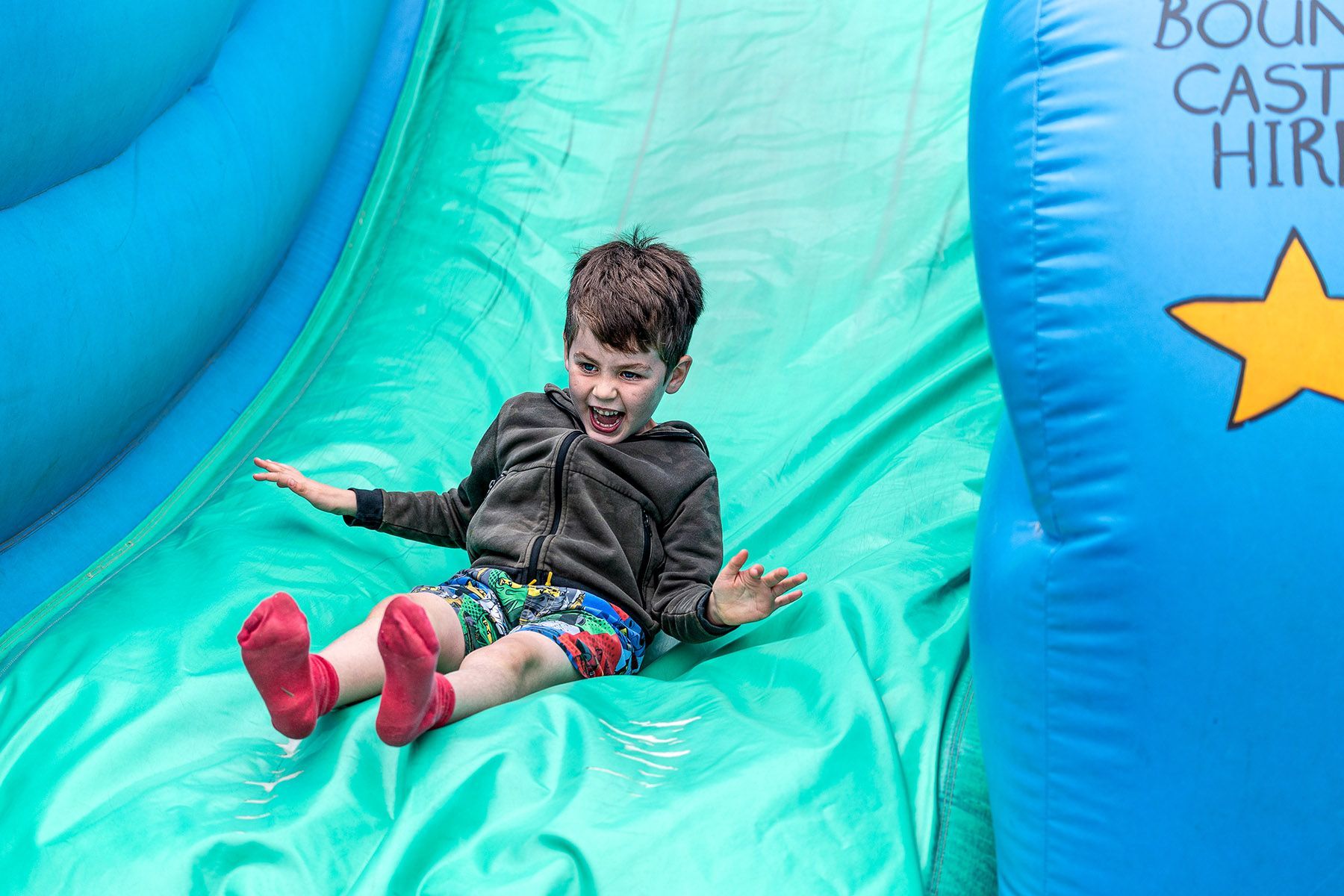 A young boy can't contain his excitement coming down a big inflatable slide!