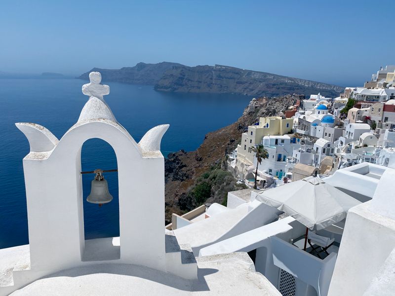 Weiße kykladische Kirche mit blauer Kuppel auf Santorini, im Hintergrund die steilen Klippen und das tiefblaue Meer.