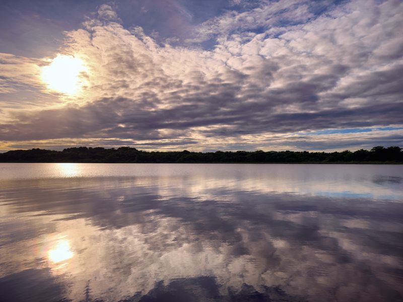 Sonnenaufgang über einer ruhigen Lagune in Belize, bei dem sich Wolken und Licht im spiegelglatten Wasser reflektieren.