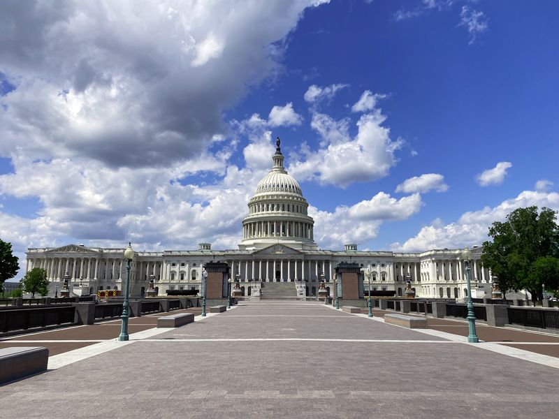 Frontalansicht des Kapitols in Washington D.C. unter einem Himmel mit weißen Wolken, aufgenommen vom breiten Weg vor dem Gebäude
