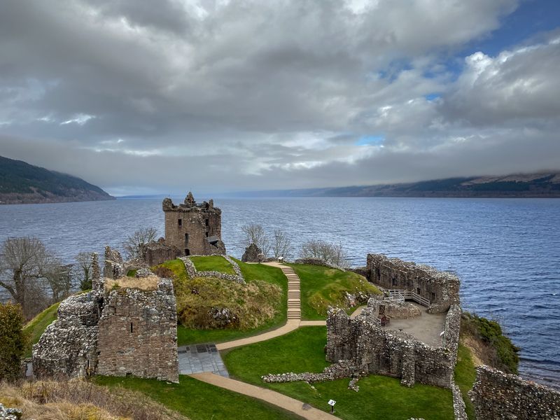 Das Eilean Donan Castle steht auf einer kleinen Insel im Loch Duich, umgeben von Bergen und einem bewölkten, stimmungsvollen Himmel.