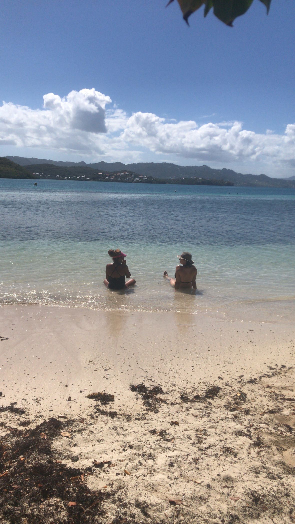 Moment de détente à deux sur la plage, face aux eaux turquoise des fonds blancs de la Martinique Deux personnes assises sur la plage, admirant les fonds blancs de la Martinique sur la côte Atlantique