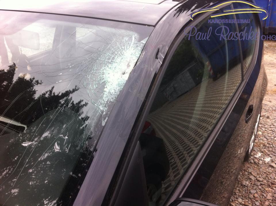 Auf dem Bild ist ein schwarzes Auto zu sehen, welches einen Sturmschaden auf der Windschutzscheibe besitzt.