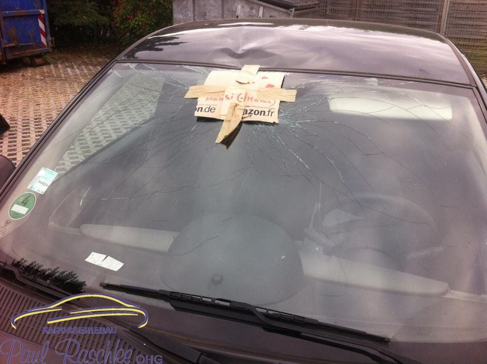 Auf dem Bild ist ein schwarzes Auto zu sehen, welches einen Sturmschaden auf der Windschutzscheibe besitzt.
