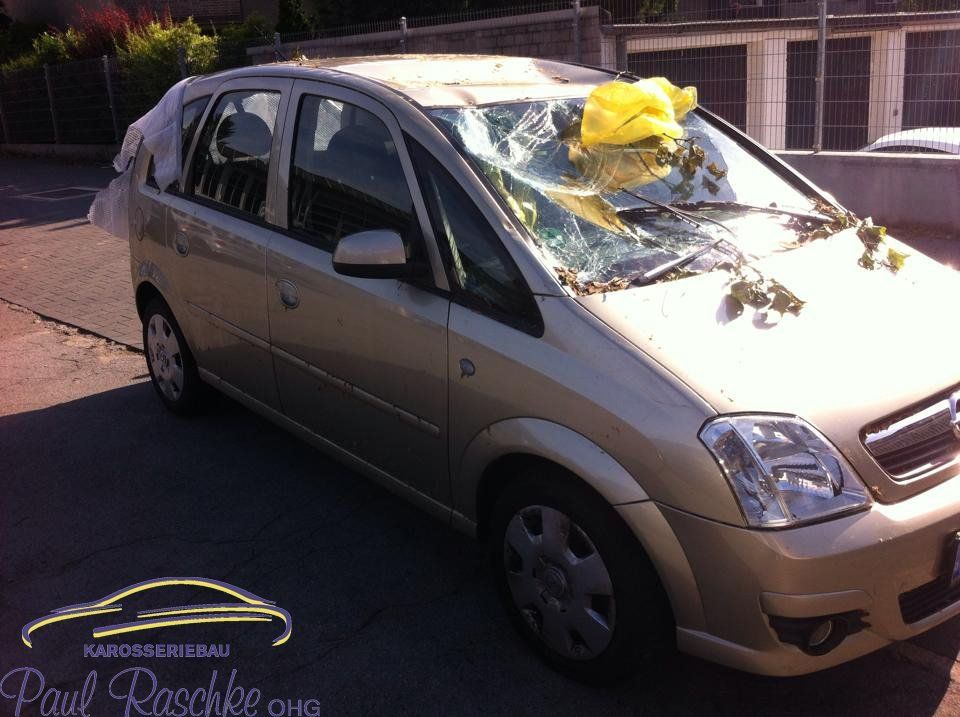 Auf dem Bild ist ein silbernes Auto zu sehen, welches einen Sturmschaden auf dem Dach und der Windschutzscheibe besitzt.