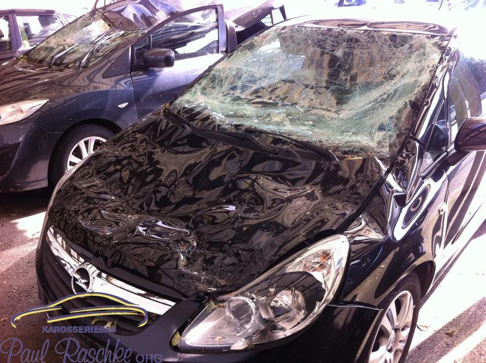 Auf dem Bild ist ein schwarzes Auto zu sehen, welches einen Sturmschaden auf der Haube und der Windschutzscheibe besitzt.