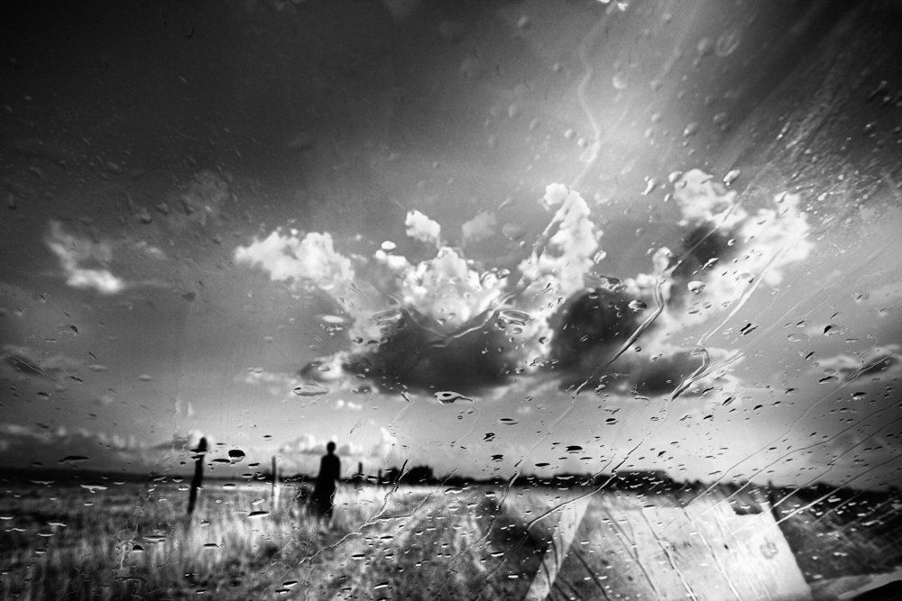 De l'autre côté du miroir : série de photographie noir et blanc de paysage, femme et silhouette sous la pluie, dans un paysage de campagne, routes désertes, ciel nuageux, orageux