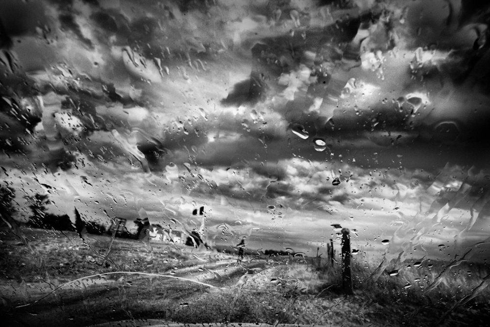 De l'autre côté du miroir : série de photographie noir et blanc de paysage, femme et silhouette sous la pluie, dans un paysage de campagne, routes désertes, ciel nuageux, orageux
