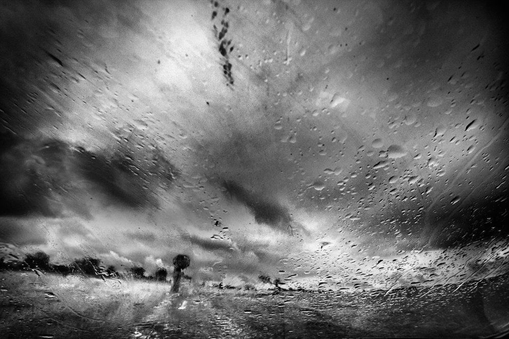 De l'autre côté du miroir : série de photographie noir et blanc de paysage, femme  et silhouette sous la pluie, dans un paysage de campagne, routes désertes, ciel nuageux, orageux