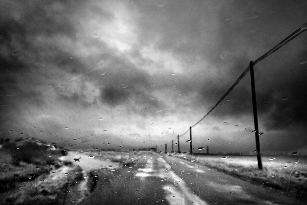 De l'autre côté du miroir : série de photographie noir et blanc de paysage, femme et silhouette sous la pluie, dans un paysage de campagne, routes désertes, ciel nuageux, orageux