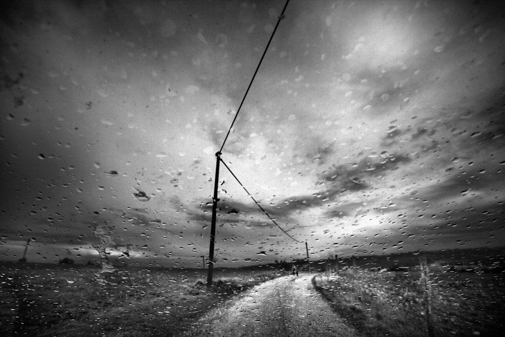 De l'autre côté du miroir : série de photographie noir et blanc de paysage, femme et silhouette sous la pluie, dans un paysage de campagne, routes désertes, ciel nuageux, orageux