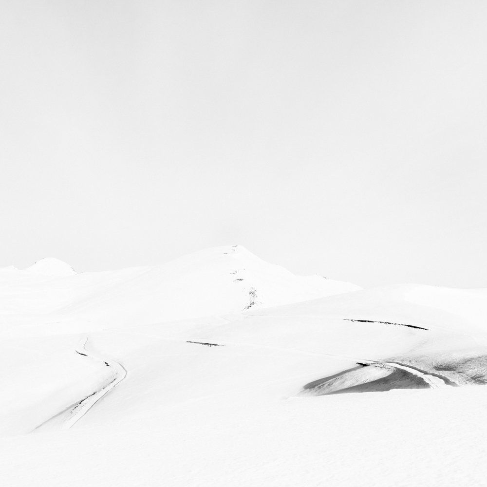 There is human beings - Il y a toujours des êtres humains : série de photographies noir et blanc épurées de paysage de montagne sous une neige blanche et pure, avec quelques traces de végétation ou de terre