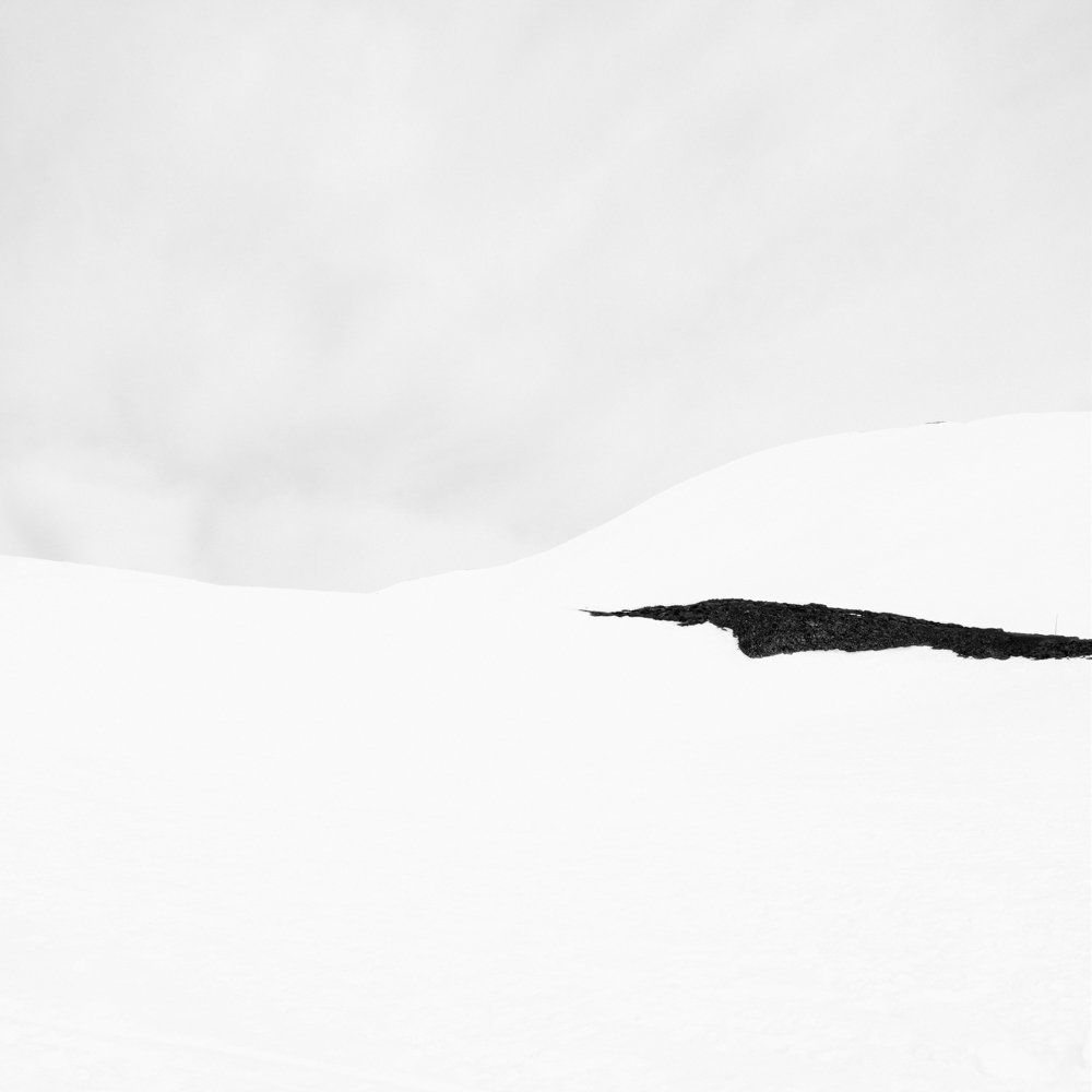 There is human beings - Il y a toujours des êtres humains : série de photographies noir et blanc épurées de paysage de montagne sous une neige blanche et pure, avec quelques traces de végétation ou de terre