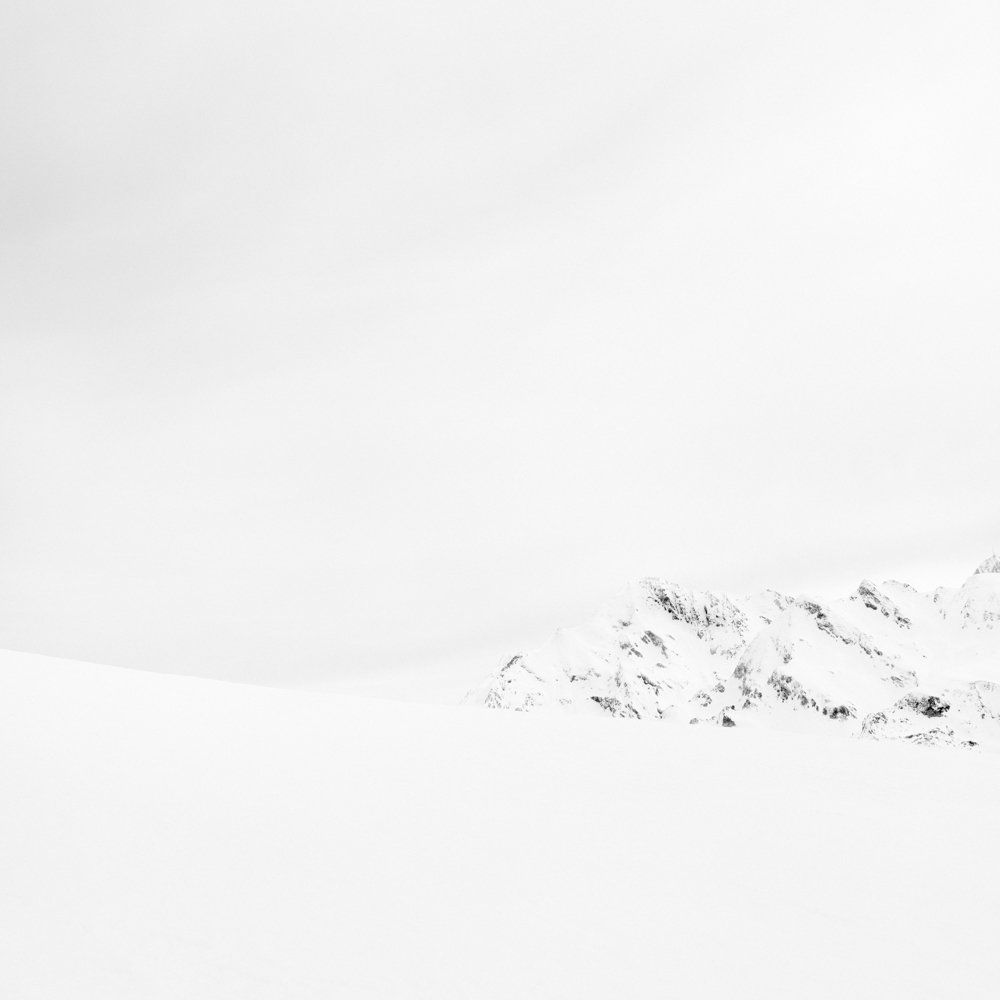 There is human beings - Il y a toujours des êtres humains : série de photographies noir et blanc épurées de paysage de montagne sous une neige blanche et pure, avec quelques traces de végétation ou de terre