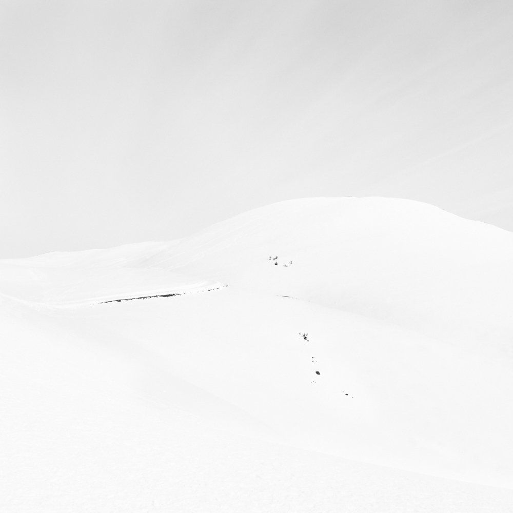 There is human beings - Il y a toujours des êtres humains : série de photographies noir et blanc épurées de paysage de montagne sous une neige blanche et pure, avec quelques traces de végétation ou de terre