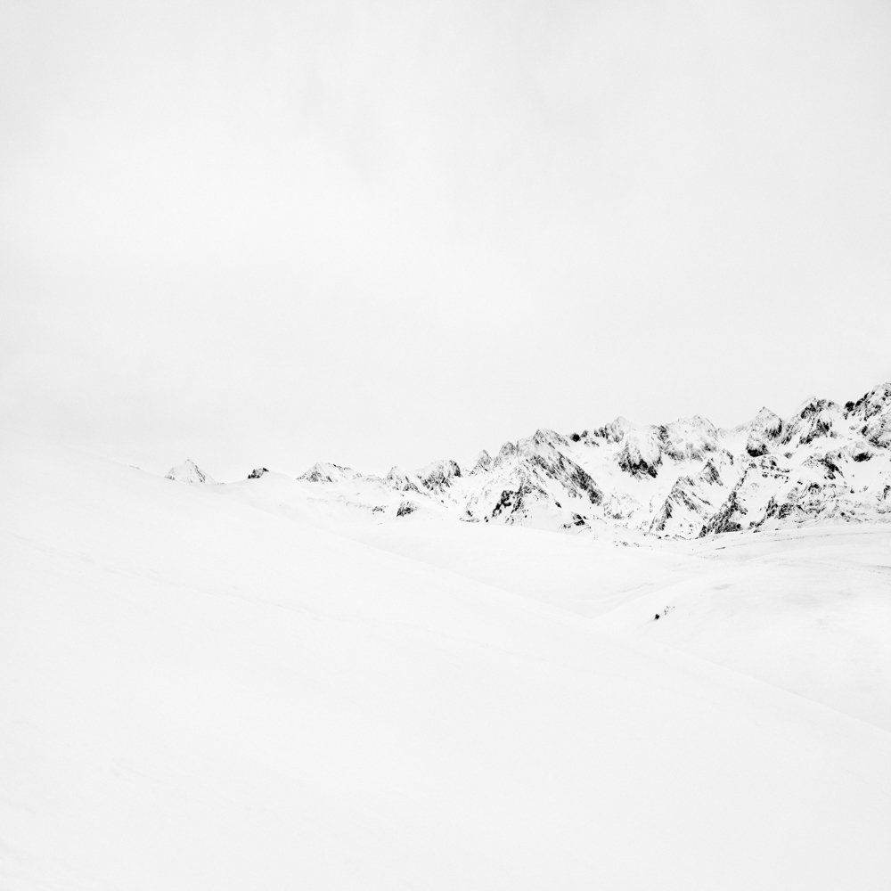 There is human beings - Il y a toujours des êtres humains : série de photographies noir et blanc épurées de paysage de montagne sous une neige blanche et pure, avec quelques traces de végétation ou de terre