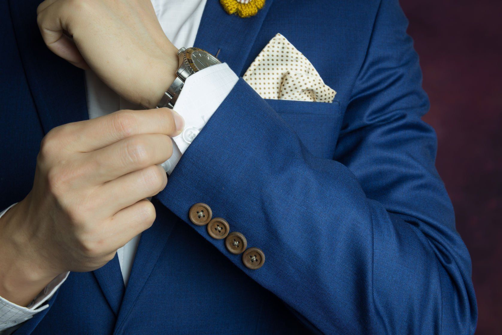 Man in a blue suit adjusting his shirt cuff.