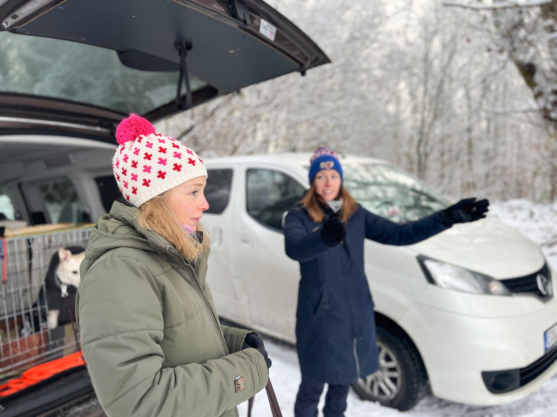 Zwei Menschen stehen vor einem Auto mit Hund drin. Die Hundetrainerin erklärt etwas.