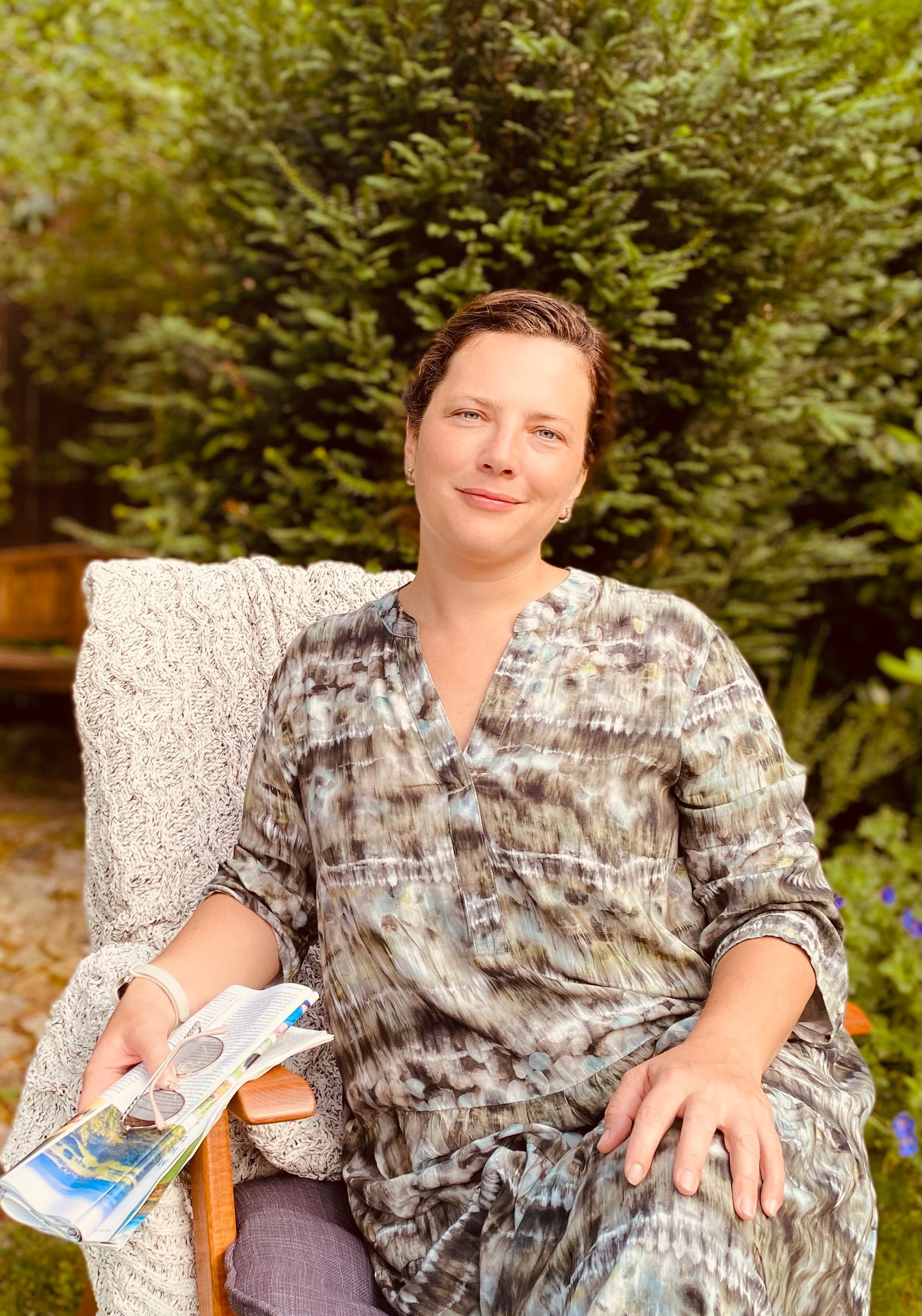 Portrait einer Frau im Sessel mit Zeitschrift und Brille in der Hand