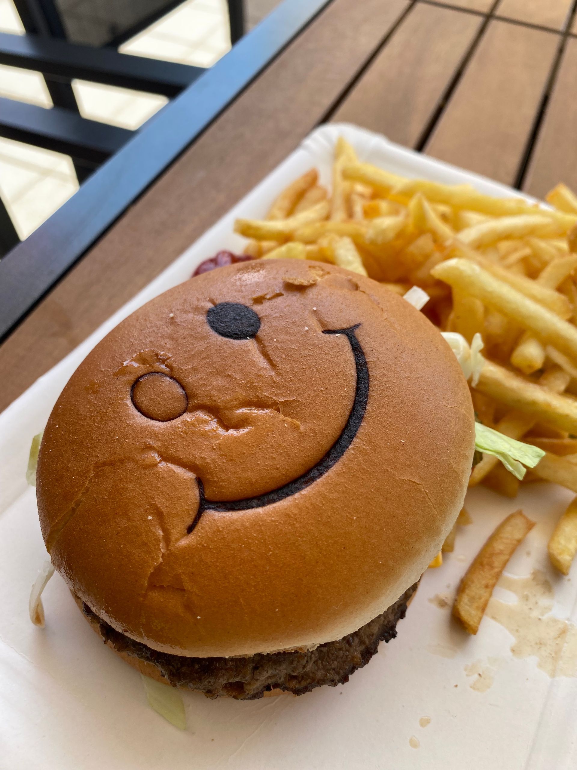 Burger mit lächelndem Gesicht und Pommes auf einem Teller auf einem Holztisch