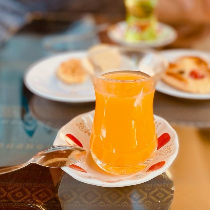 Kleines Glas mit orangenem Getränk und Gebäck auf kleinen Tellern