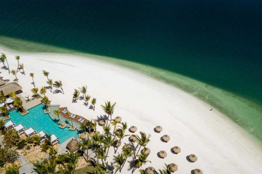 Aerial view of a white sand beach resort with palm trees and turquoise ocean water