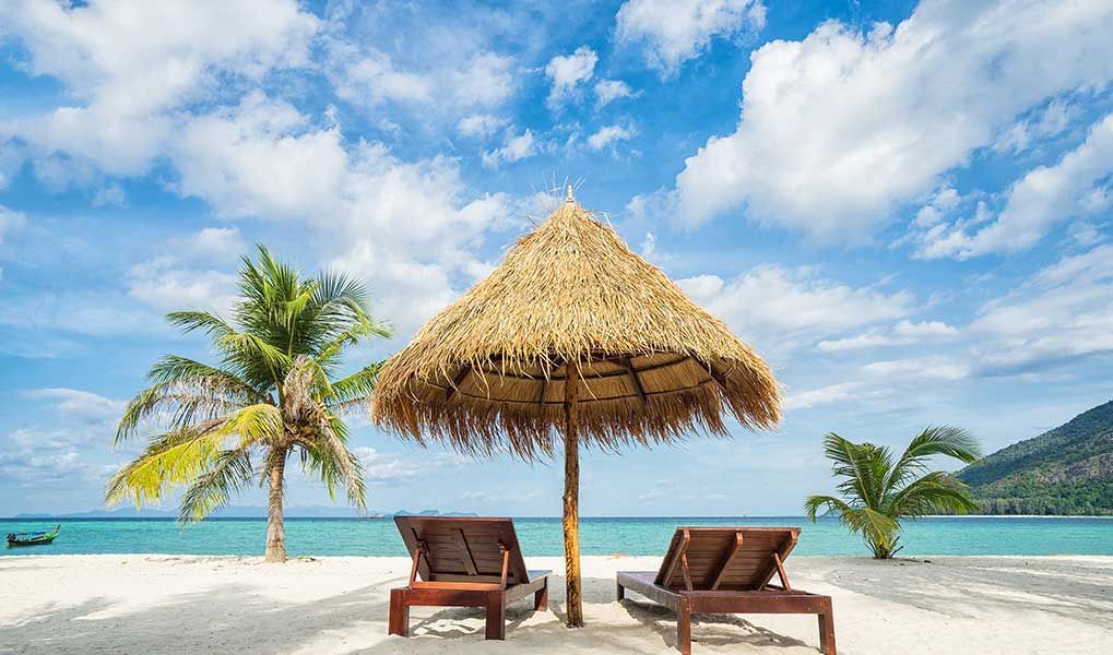 Sun loungers beneath a thatched umbrella on a peaceful tropical beach. Sun loungers beneath a thatched umbrella on a peaceful tropical beach.