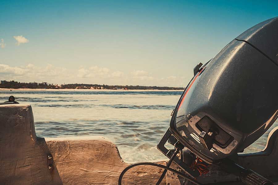 Close-up of a boat's outboard motor with the ocean and coastline visible behind Close-up of a boat's outboard motor with the ocean and coastline visible behind