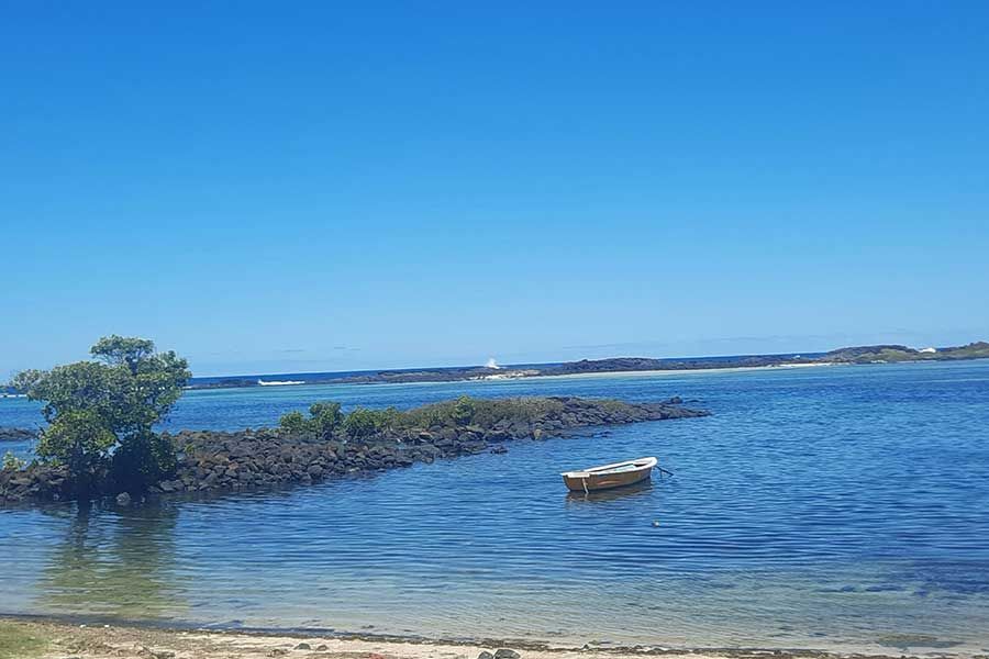 Small boat anchored in a calm bay near a rocky breakwater in Mauritius Small boat anchored in a calm bay near a rocky breakwater in Mauritius